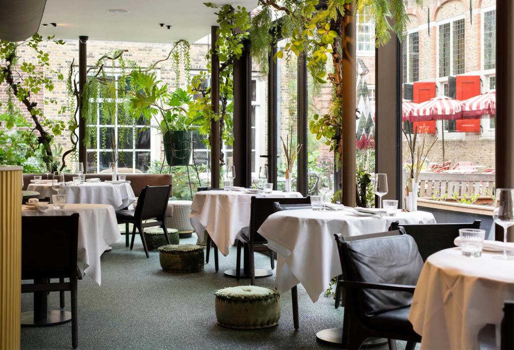 um restaurante com mesas e cadeiras brancas e janelas em Relais & Châteaux Weeshuis Gouda em Gouda