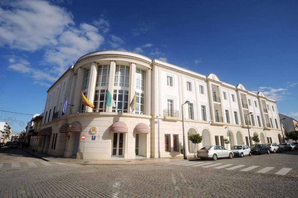 un grand bâtiment blanc avec des voitures garées devant lui dans l'établissement Hotel Castillo, à Palma del Río