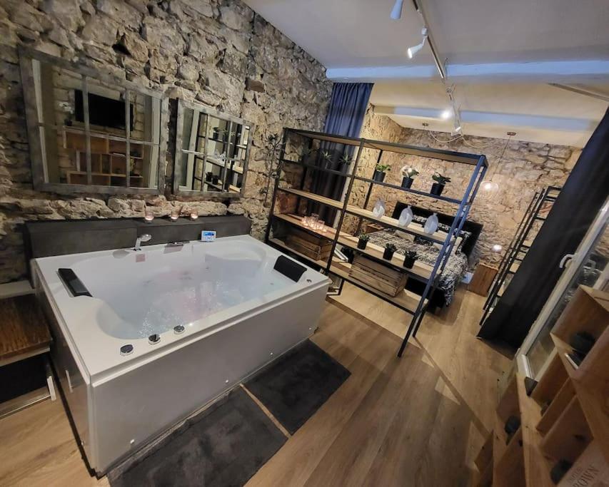 eine große Badewanne in einem Zimmer mit einer Steinmauer in der Unterkunft Le 79 Balnéo Loft Déco Authentique Centre climatisation in Sète
