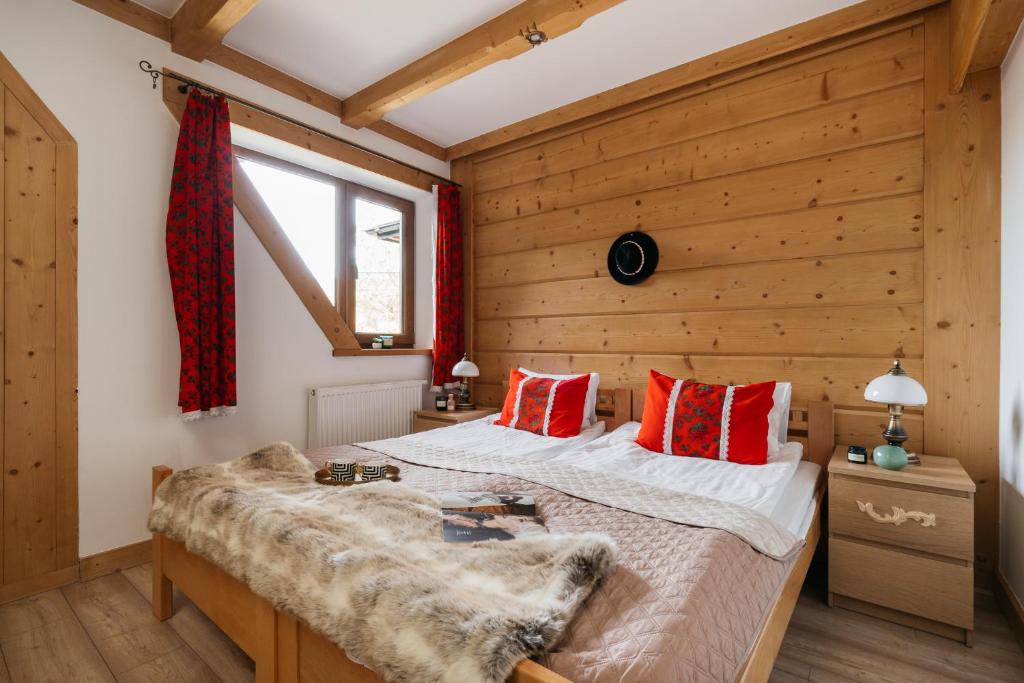 a bedroom with wooden walls and a bed with red pillows at Apartament Skibówki by LoftAffair in Zakopane