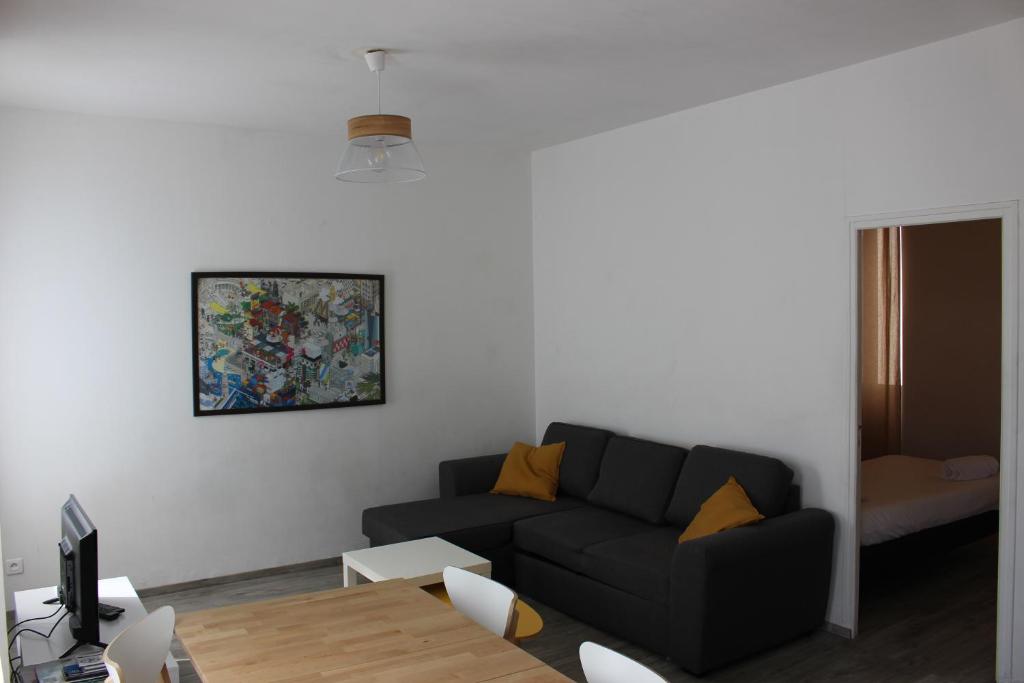 ein Wohnzimmer mit einem schwarzen Sofa und einem Gemälde an der Wand in der Unterkunft Bienvenus à Thèse - Appartement Orange in Marseille