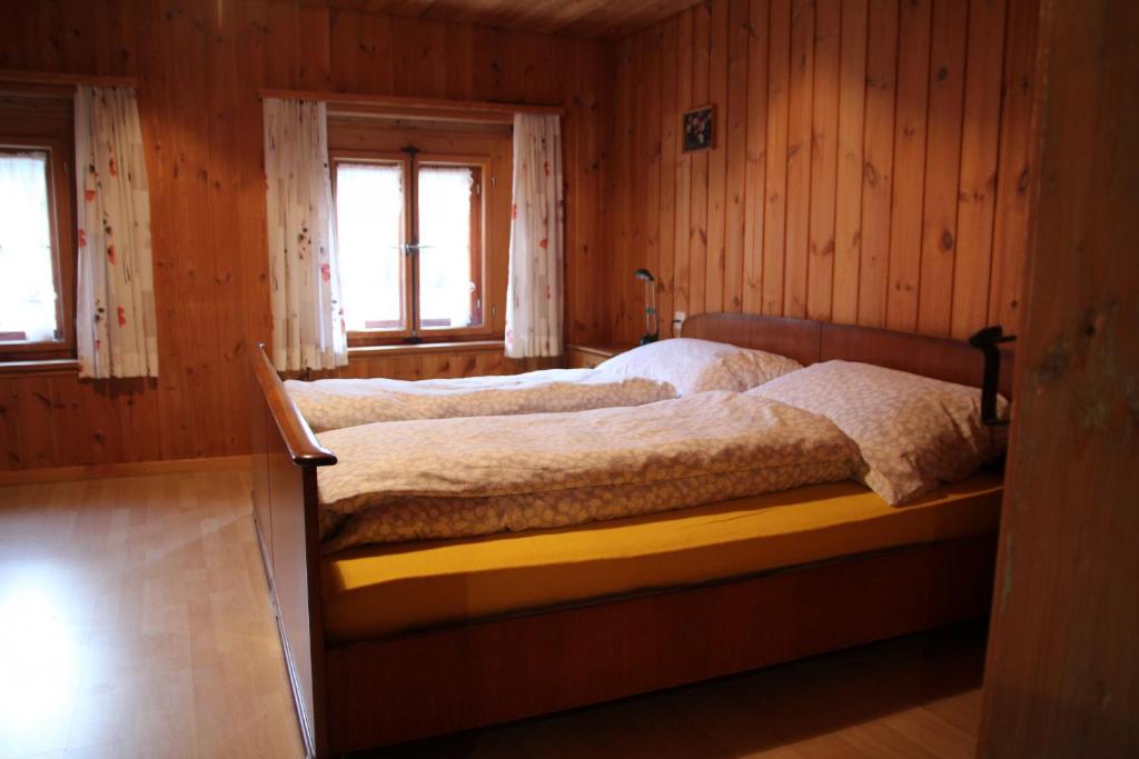 Bett in einem Holzzimmer mit zwei Fenstern in der Unterkunft Chasa Campell in Ardez