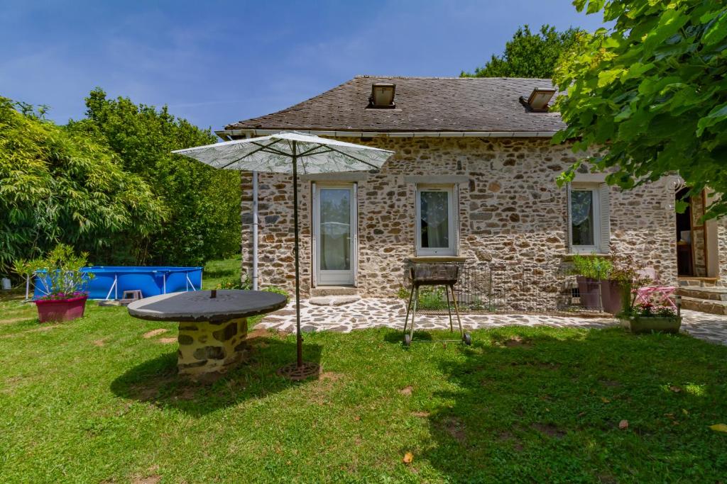 une maison en pierre avec une table et un parasol dans l'établissement Gite Loucastan, à Lagraulière