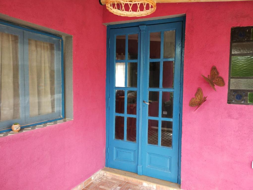 un edificio rosa con una puerta azul y mariposas en él en Sankofa Cabañas en Yacanto