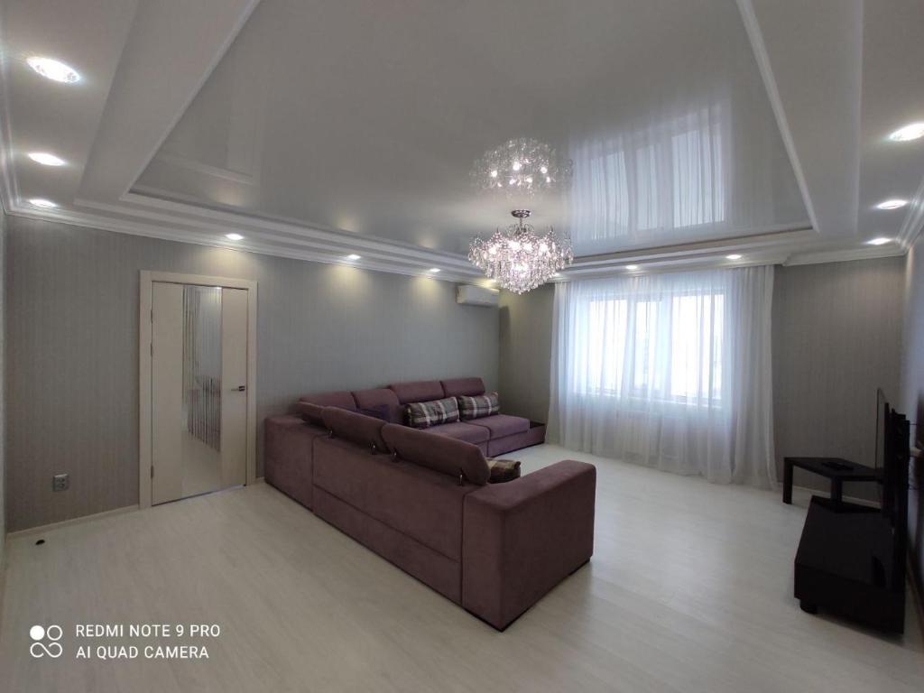 een grote woonkamer met een bank en een kroonluchter bij Уютная квартира на Кадыр-Мырза Али in Oral