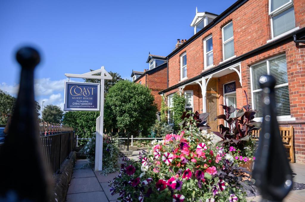 a sign in front of a house with flowers at Coast Guest House in Whitby