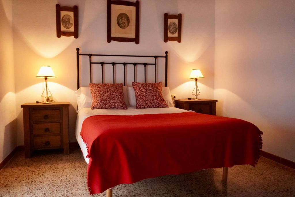 Casa Rural Sierra Tórtola 1 في Hinojales: غرفة نوم بسرير وبطانية حمراء ومصباحين