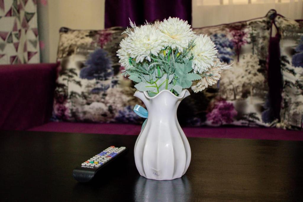 a white vase with flowers on a table next to a remote control at Arctic tern homes in Embu