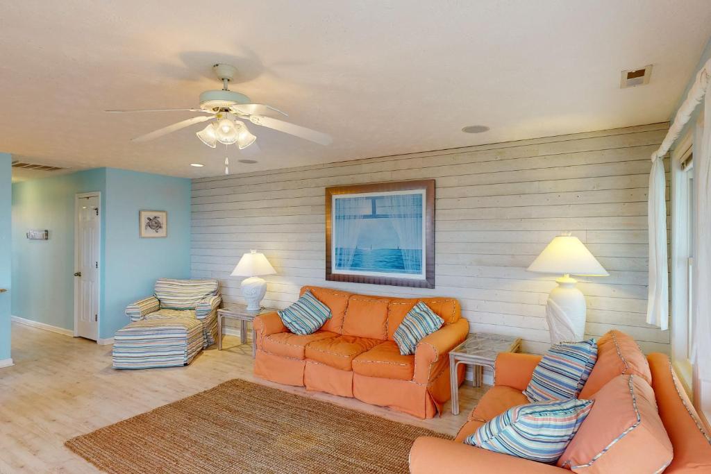 sala de estar con muebles de color naranja y ventilador de techo en Home by the Sea en Surf City