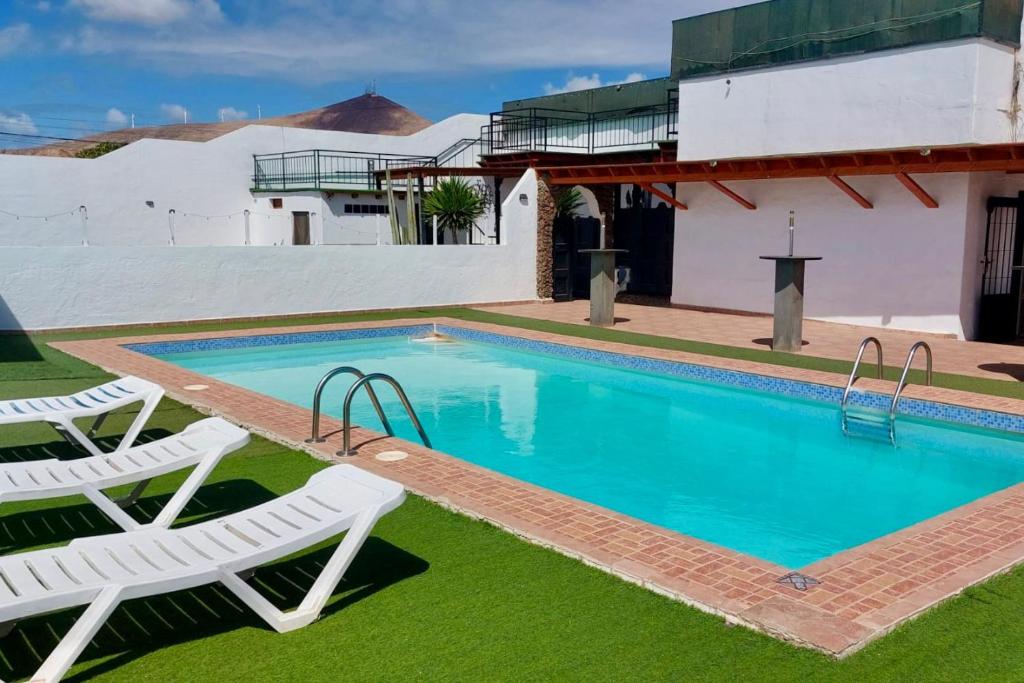 a swimming pool with two lawn chairs and a house at Lanzarote Hostel in Arrecife