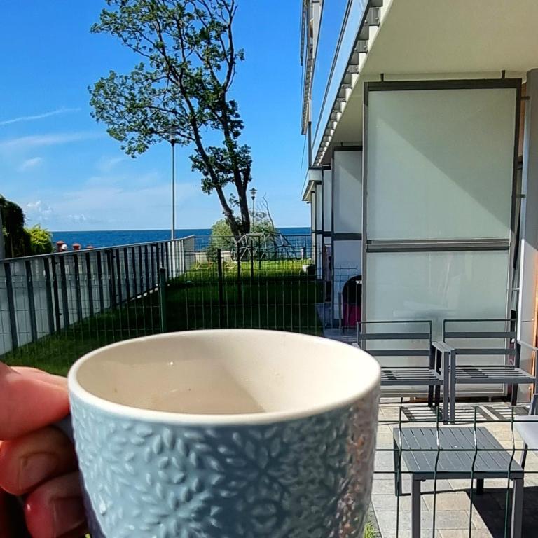 a person holding a cup with the ocean in the background at Apartament Dar Pomorza 20m do Plaży Ustronie Apartments in Ustronie Morskie