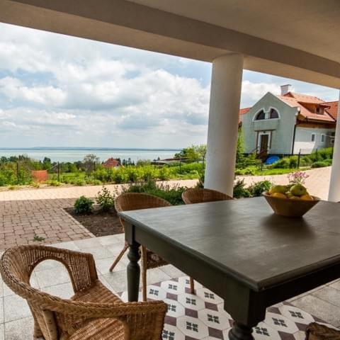 a table with chairs and a bowl of fruit on a porch at Villa Portico in Badacsonytomaj