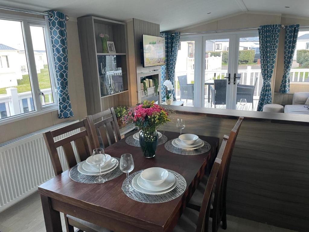 Luxury Romantic 2 Bedroom Caravan Trecco Bay في Newton: طاولة غرفة الطعام مع الأطباق والزهور عليها