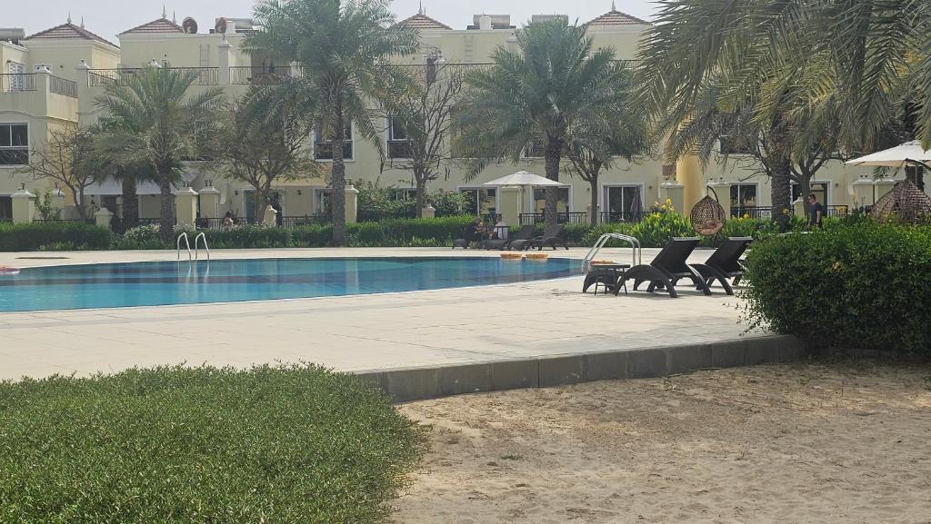 a swimming pool with chairs and a table next to a building at Luxury villa 4 bedroom with pool access in Ras al Khaimah