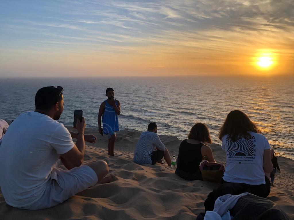 een groep mensen die op het strand zitten en naar de zonsondergang kijken bij Oceana surf house in Imsouane