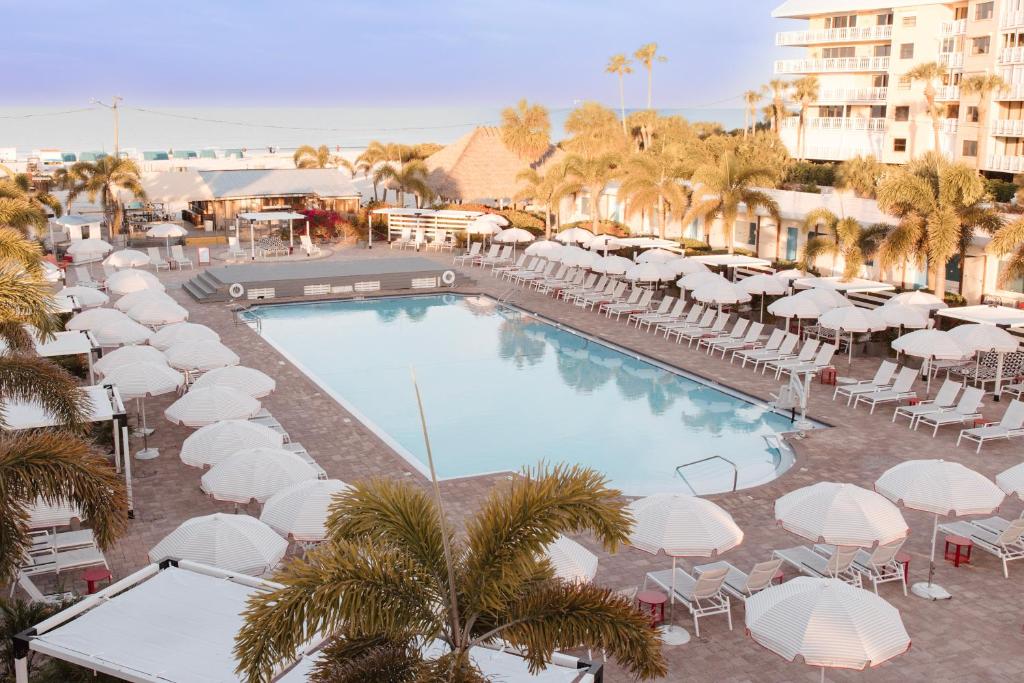 uma piscina com guarda-sóis brancos, mesas e cadeiras em Postcard Inn On The Beach em St. Pete Beach