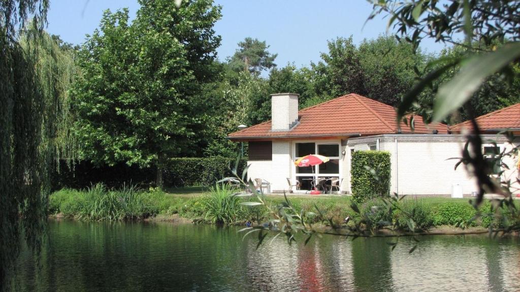 una casa blanca con techo rojo junto a un lago en Bungalows für vier Personen, direkt am Strandbad gelegen, en Oostrum