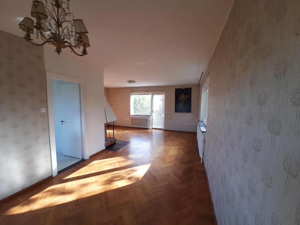 een lege kamer met een houten vloer en een kroonluchter bij Room in house with good communication in Stockholm