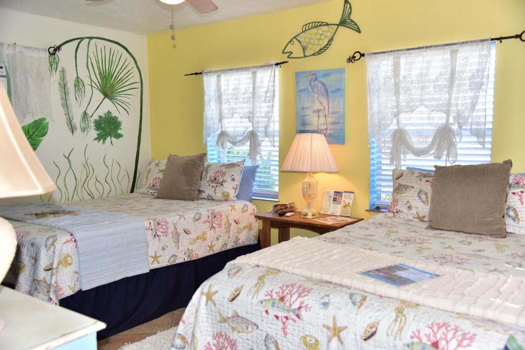 two beds in a room with yellow walls and windows at SI COMO NO INN in Flagler Beach