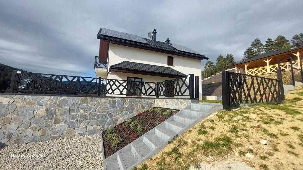 a white house with a black roof and a stone wall at Apartamenty TRIO in Muszyna