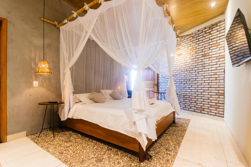 1 dormitorio con cama con dosel y pared de ladrillo en Villa Malie, en Santo Amaro