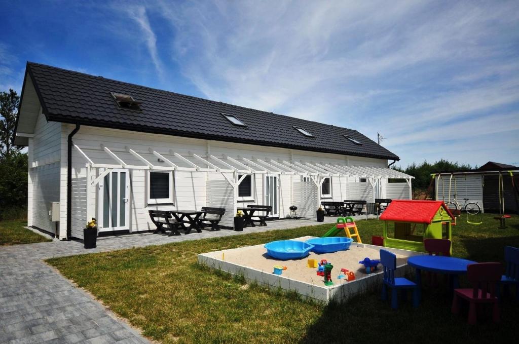 um edifício branco com uma caixa de areia e uma casa de brincar em Gemütliches Ferienhaus in Grzybowo mit Garten, Terrasse und Grill - b53705 em Grzybowo