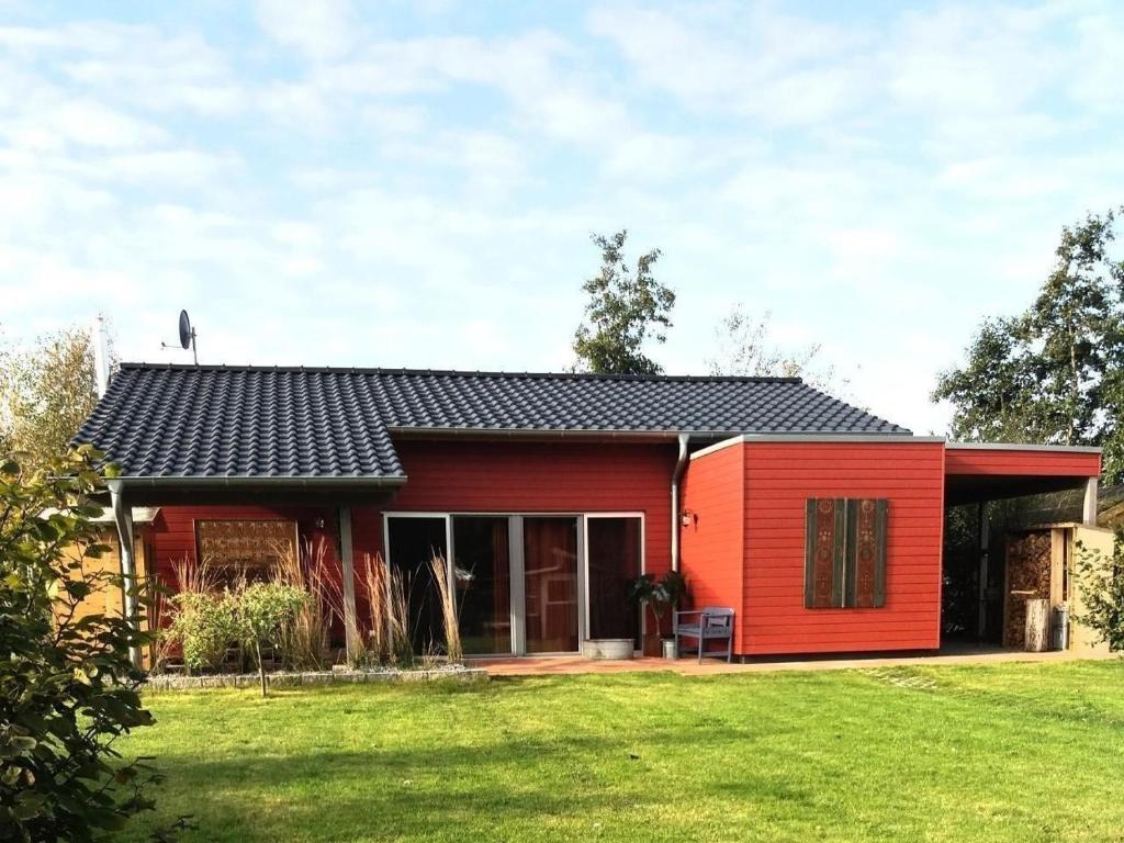 a red house with a black roof and a yard at Ferienhaus am kleinen See mit Steg, Garten und Terrasse in Twist
