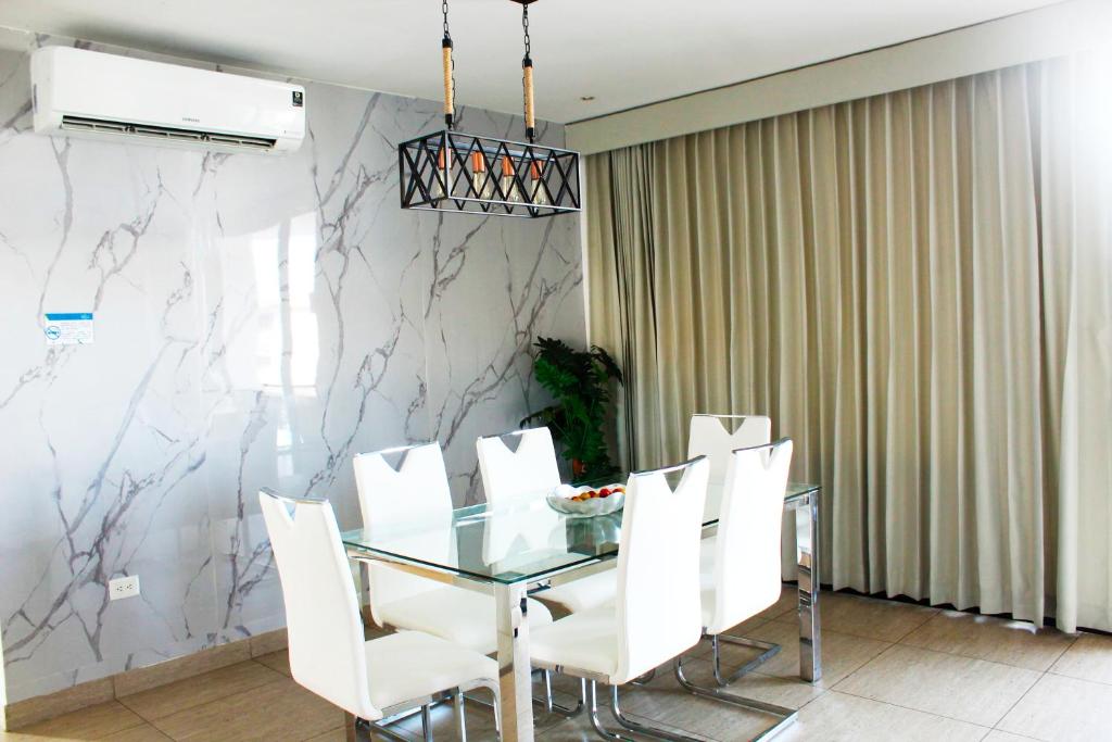 The Luxury Apartment في سان سلفادور: غرفة طعام مع طاولة زجاجية وكراسي بيضاء