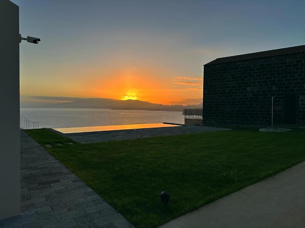 a sunset over the water with a brick building and grass at João de Oliveira casas de campo in Santo António