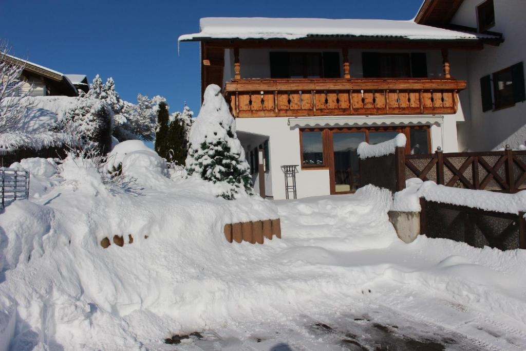 une maison recouverte de neige devant une maison dans l'établissement Schönes Ferienhaus in Lechbruck Am See mit Großer Terrasse und Bergblick, à Lechbruck am See