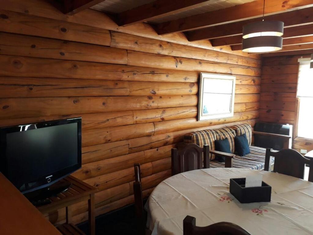 Habitación con paredes de madera, TV y mesa. en cabaña junto al arroyo en San Martín de los Andes