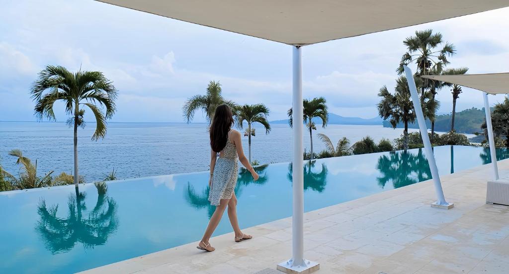 a woman walking by a swimming pool overlooking the ocean at Shunyata Villas Bali in Seraya
