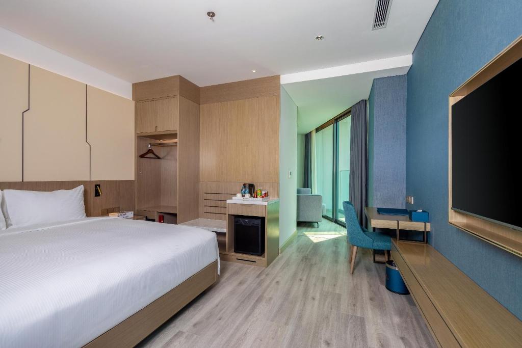 A furnished room with a large bed, television, compact work desk and bright glazed sitting area.