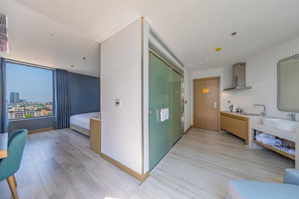 An open-plan room showing a city view, bed, glazed bathroom and kitchenette-style storage.