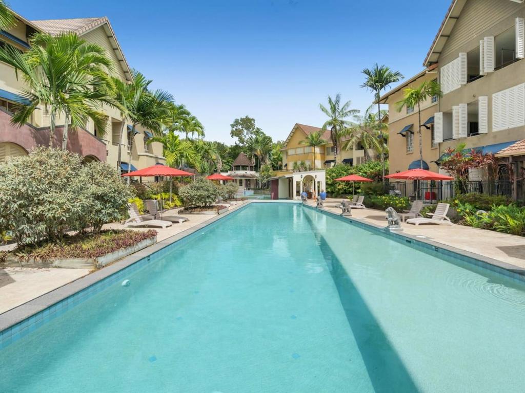 una piscina en un complejo con palmeras y sombrillas en Discover a Lush Poolside Stay at The Lakes Resort, en Cairns North