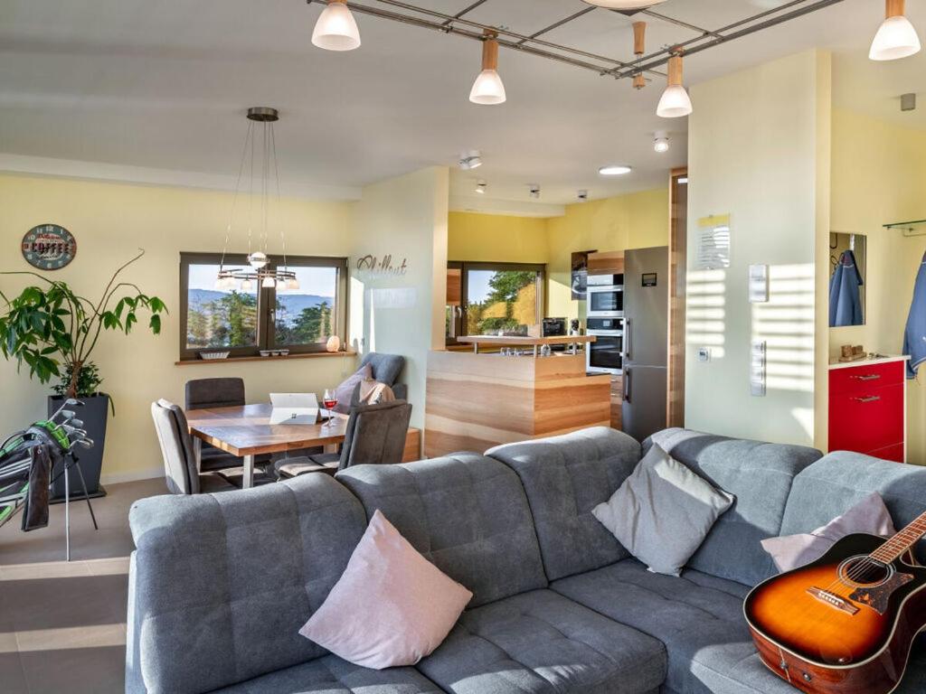 ein Wohnzimmer mit einem grauen Sofa und einer Gitarre in der Unterkunft Mosel Sky Lounge with loggia & panoramic view in Kenn