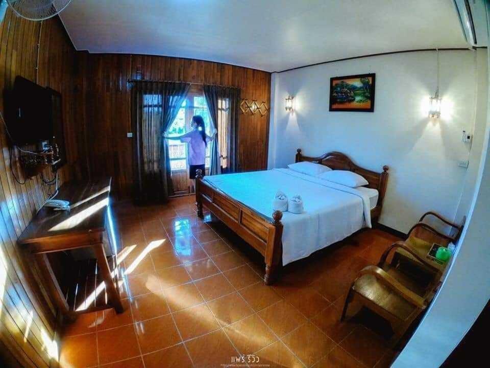 - une chambre avec un lit et une personne debout sous la fenêtre dans l'établissement บ้านสวนกุหลาบแก้วรีสอร์ท, à Ban Mae Lai