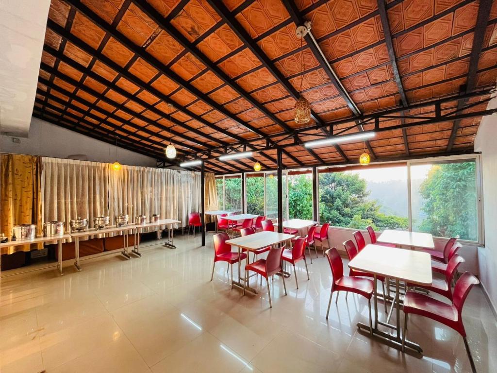 un restaurante con mesas, sillas rojas y ventanas en Red Stone Villas en Madikeri