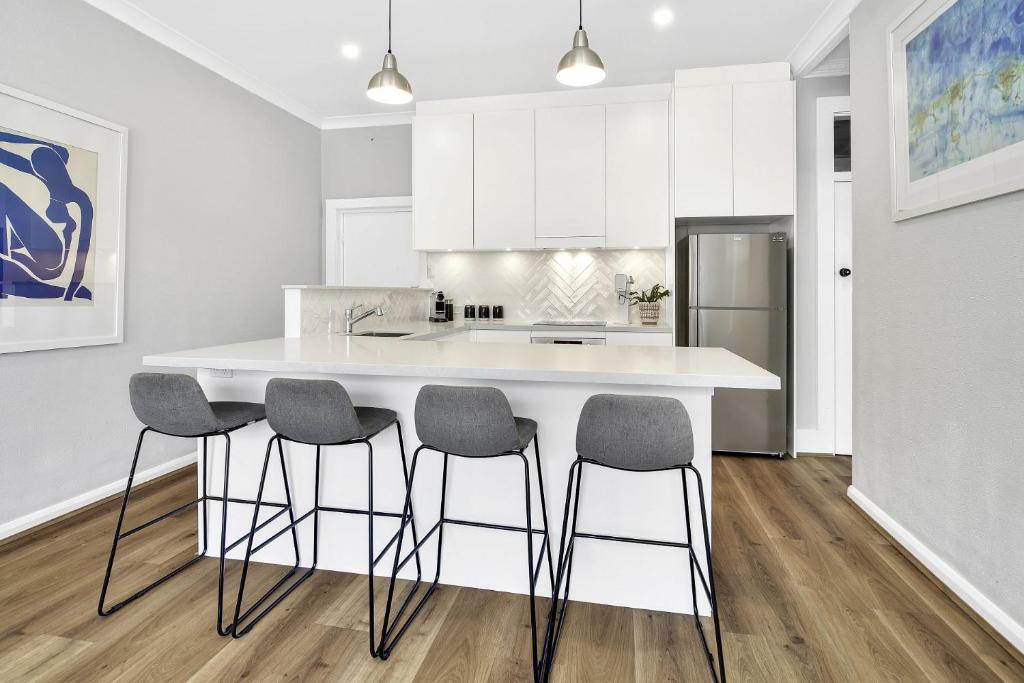 a kitchen with a large white island with four bar stools at Stylish, Sunny & Spacious 2 Bedroom Apartment, Mosman in Sydney