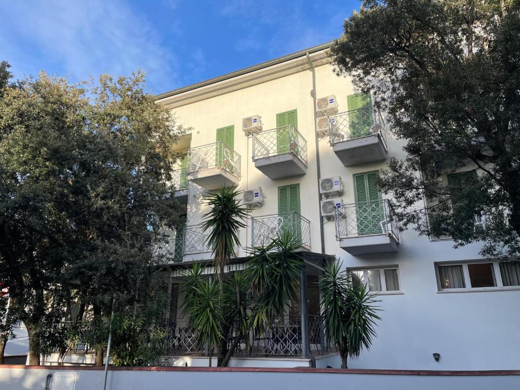 un edificio blanco con ventanas con contraventanas verdes y palmeras en Hotel l'Etrusco - San Vincenzo, en San Vincenzo