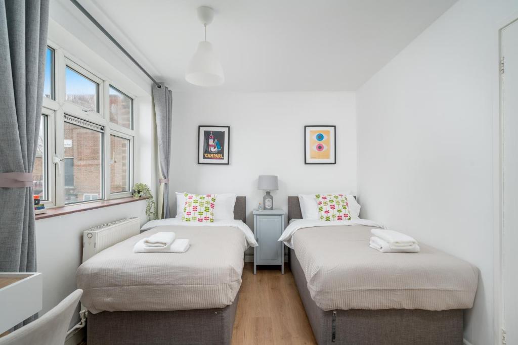two twin beds in a room with two windows at Luxe 3 Bedroom flat In London on Central Line for Families, Contractors, Business Travellers in Woodford Green