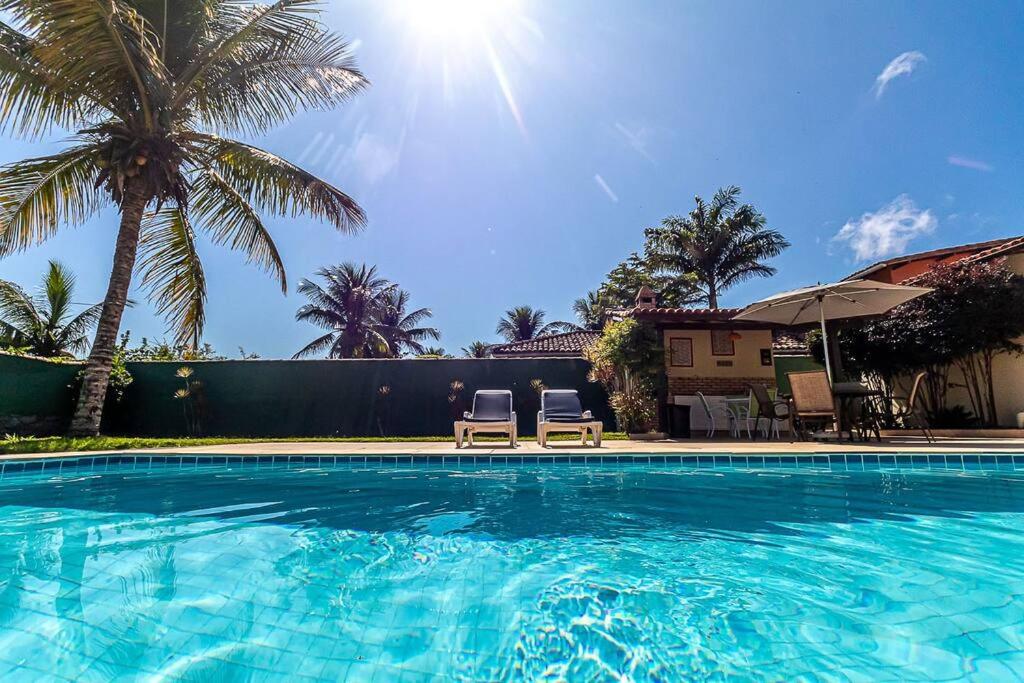 a swimming pool with two chairs and palm trees at Linda casa em Búzios a 50 m da Praia da Ferradura. in Búzios