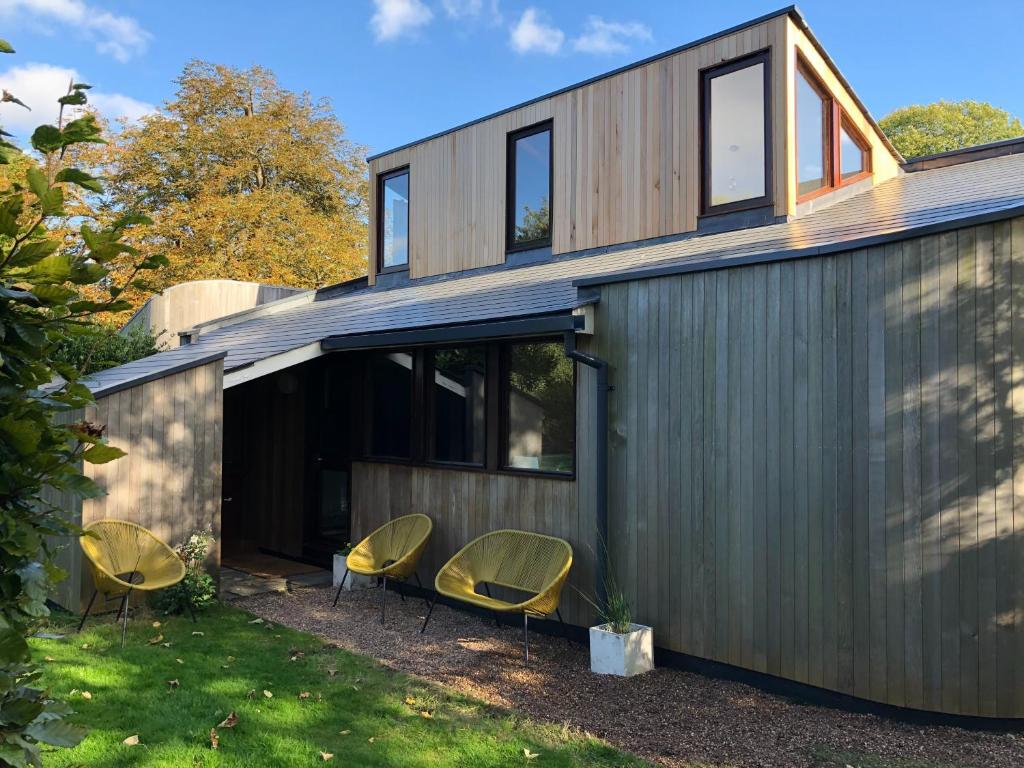 a house with three chairs sitting in the yard at A Unique, Rural, Modern Annexe with Large Garden, Games, Tennis Court & EV Point in Chichester