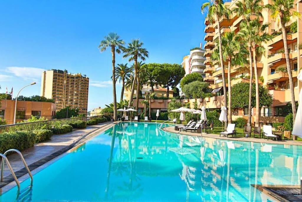 a swimming pool with palm trees and a building at Luxurious Monaco Flat: Stunning Views & Amenities in Monte Carlo
