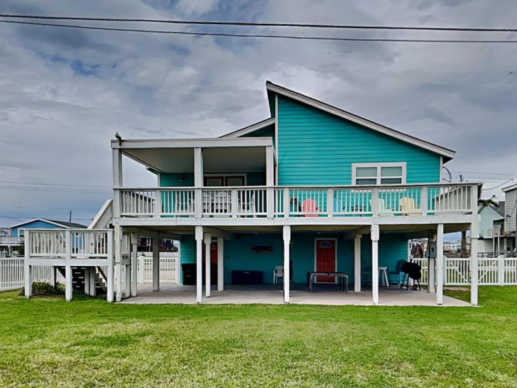 a blue house with a white deck and grass at Seagulls Landing in Galveston