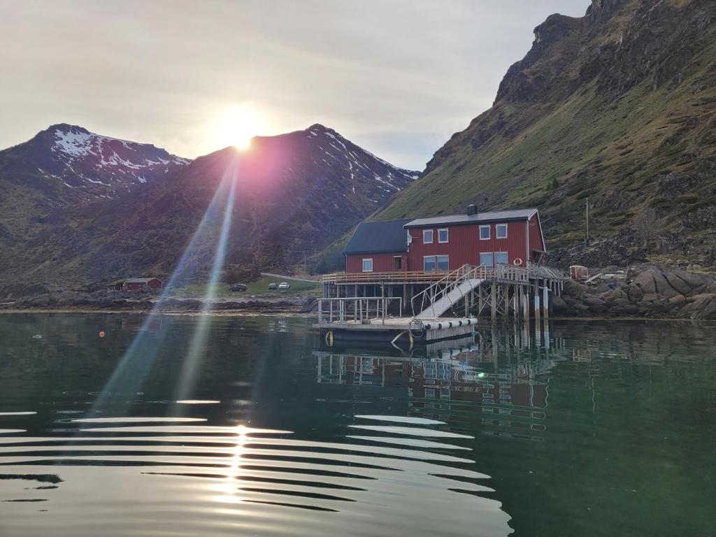 a red house on a dock on the water with mountains at Solodden, Authentic rorbu in Lofoten in Sennesvik