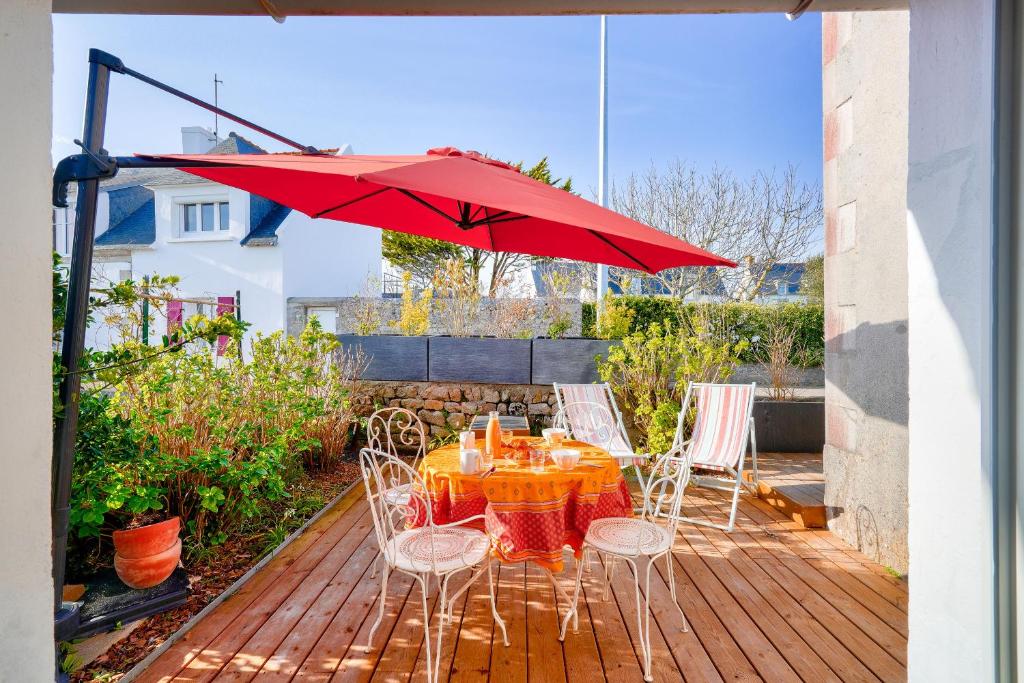 a table and chairs with a red umbrella on a deck at À 700m de la plage, charmante maison pour 6 in Kersuluan