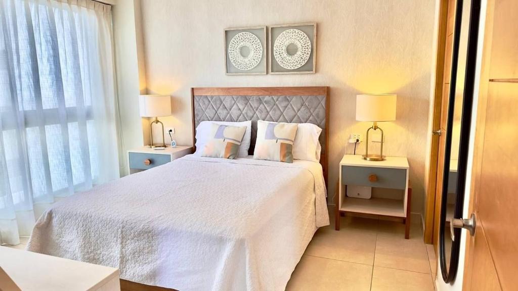 um quarto com uma grande cama branca e 2 candeeiros em Bello apartamento en Evaristo Morales, 1 BR em Santo Domingo