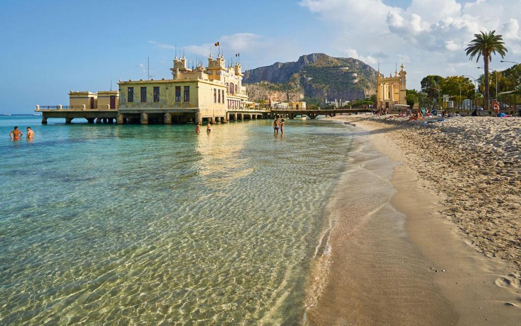 a beach with a building and people in the water at Villa Strazzeri in Palermo