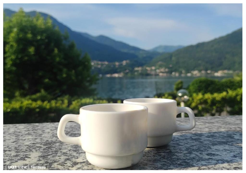 two white coffee mugs sitting on a table with a view at LFSUITE LuganoLake Terrazza Spiaggia privata Parking WI-FI Netflix in Porlezza